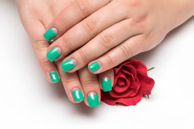 yeşil, nane ay manikürü, kısa kare ellerde kristaller, avuçlarında kırmızı bir gül, beyaz arka planda yakın plan.