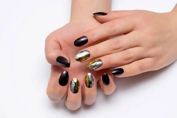 Gel nail design for Halloween. Black, shimmery, brown, silver, gold manicure on short oval nails close-up on a white background.