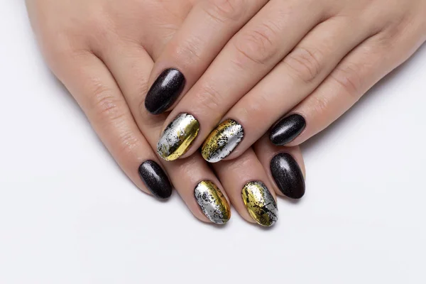 Gel nail design for Halloween. Black, shimmery, brown, silver, gold manicure on short oval nails close-up on a white background.
