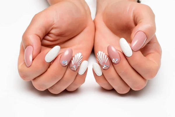 Wedding summer manicure. Drawn shell with crystals. White sequins. Delicate beige manicure on long oval nails on a white background. Summer manicure.