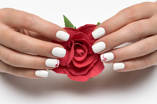 white manicure with red heart and cardiogram on a short square nails with a red rose in hands on a white background