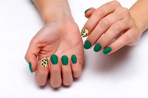 Gel nail design. Green, yellow matte with black leaves manicure on short oval nails close-up on a white background.