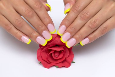 Sarı manikür, kısa kare çivilerde parıltılar, beyaz arka planda kırmızı bir gül.