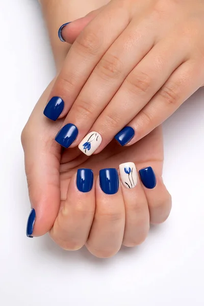 Blue manicure with a beige ringless nail and painted flowers on short square nails. Gel coating of nails. Close-up.