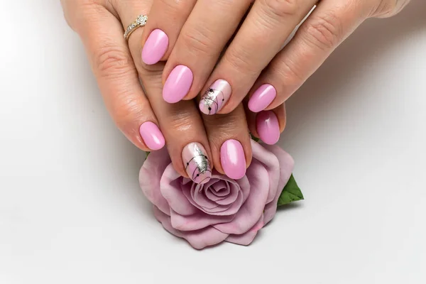 Pink manicure on oval short nails with silver foil, cobweb, brush strokes. Gently pink manicure. Silver sparkles. Well-groomed hands. Manicure with a flower, a rose in the palms.