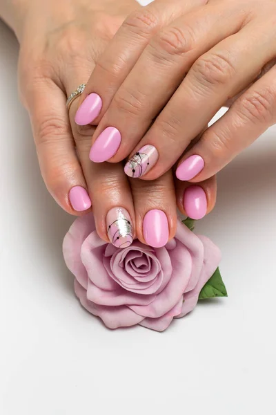 Pink manicure on oval short nails with silver foil, cobweb, brush strokes. Gently pink manicure. Silver sparkles. Well-groomed hands. Manicure with a flower, a rose in the palms.