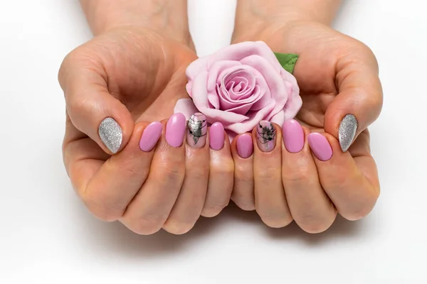 Pink manicure on oval short nails with silver foil, cobweb, brush strokes. Gently pink manicure. Silver sparkles. Well-groomed hands. Manicure with a flower, a rose in the palms.