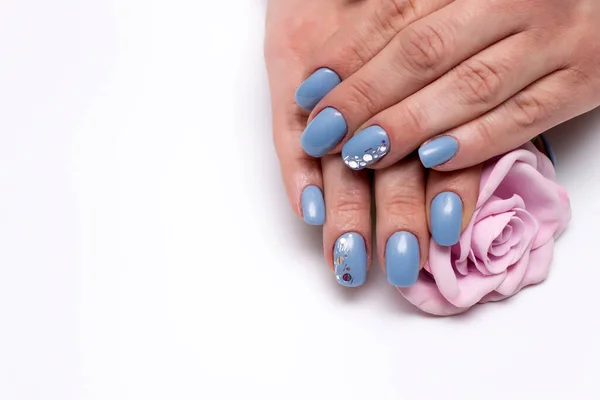 blue manicure on square long nails with sparkles on ring fingers with a pink rose in hands close-up on a white background