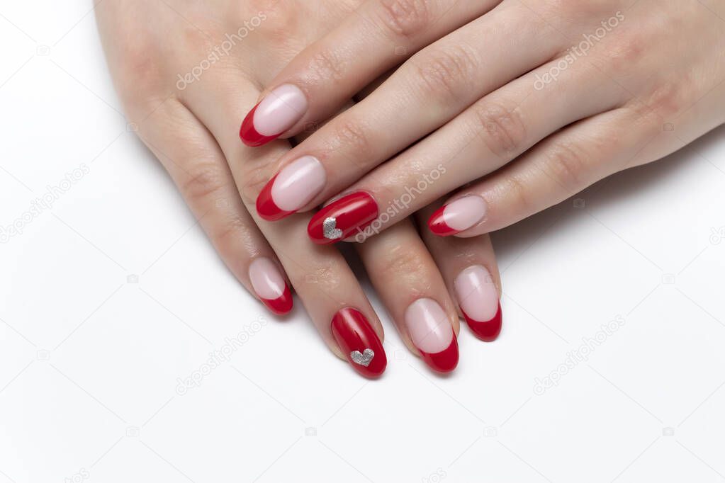Red French manicure with painted silver hearts on ring fingers on long oval nails close-up on a white background.