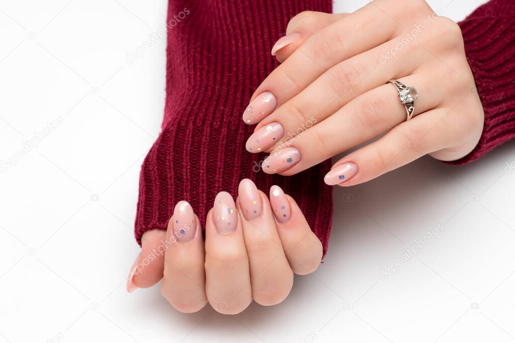 Delicate manicure with confetti on a beige background. Oval long nails with sequins. Close-up on a white background.