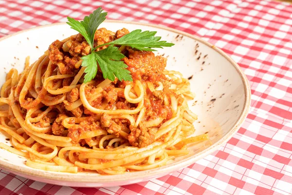 Tasty classic Italian spaghetti with bolognese and basil on a white plate on a red and white checkered tablecloth. Copy space for your text — Stock Photo, Image