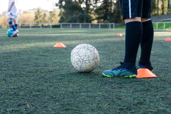 Tanımlanamayan çocuklar suni çim sahasında futbol antrenmanı yapıyorlar. İkisi de ayaklarının dibinde renkli koniler kullanarak antrenman yapmaya başlıyorlar..