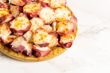 A close-up of pulpo a la gallega, an octopus with boiled potatoes typical Galician dish, on a traditional wooden plate, with copy space.