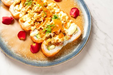 Kırmızı gül yapraklarının yanında yengeç salatalı bir tabak tempura suşi rulosu. Japon yemek menüsü kavramı.