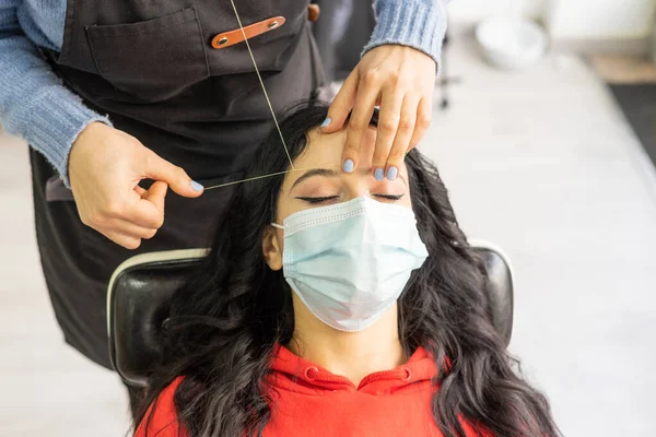 Primer plano de una parte de la cara arrancando las cejas con un hilo. Cliente con máscara — Foto de Stock