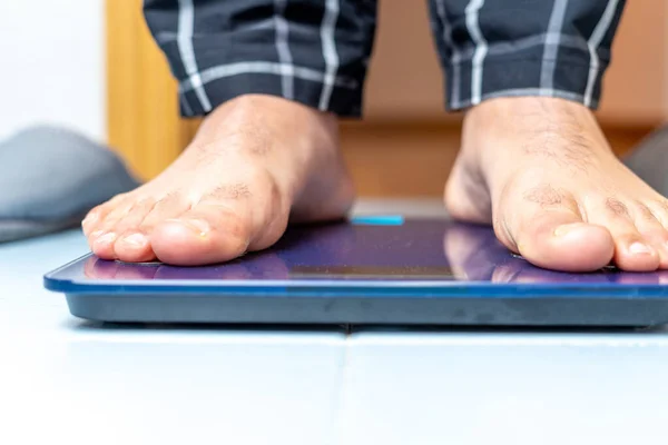 Närbild av en mogen mans fötter på en elektronisk viktvåg i badrummet hemma. Viktkontroll koncept. — Stockfoto