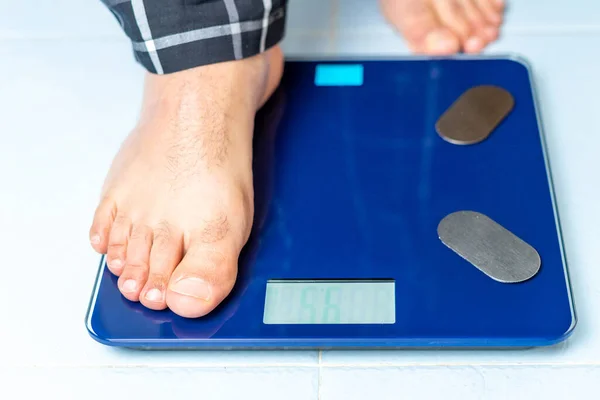 Close up of a mans feet as he first places one foot on the weight scale to start the measurement. Checkweighing concept.