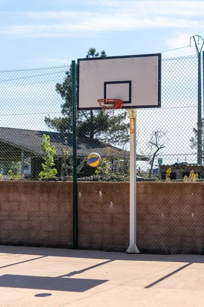 Basket backboard gör en markerad skugga bredvid en färgglad boll på en tom bana. Vertikalt skott — Stockfoto