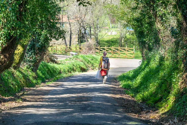 Sırt çantalı, etrafı sebze tüneliyle çevrili bir yolda yürüyen ve İspanya 'nın kuzeyinde küçük bir köye giren tanınmamış bir yolcu..