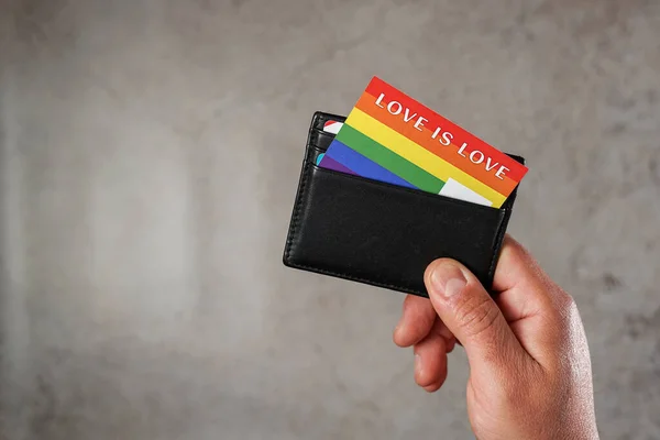 Hand of a man showing his wallet with a card with the colors of the LGBTQ movement with the phrase Love is Love. Concept of identification with the LGBTQ movement — Stockfoto