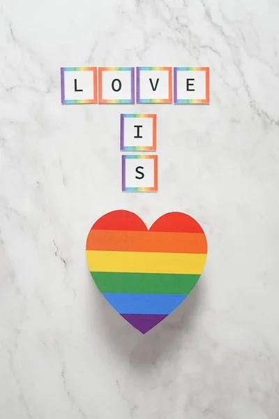Coração com as cores do movimento LGBTQ com a frase Amor é. Conceito de tolerância, inclusão e diversidade — Fotografia de Stock