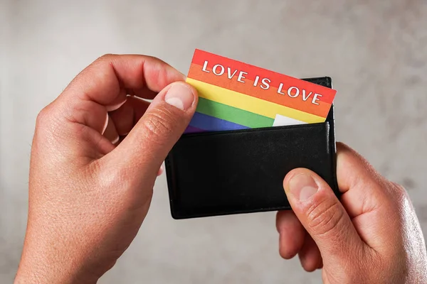 Hands of a man show a card in the colors of the LGBTQ movement with the phrase Love is Love that he takes out of his wallet. Concept of identification with the LGBTQ movement — Stockfoto