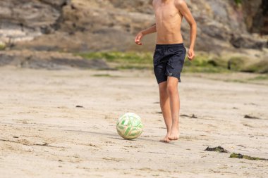 Çocuk kumsalda kumda futbol oynuyor. Tanınmayan insanlar. Yaz tatili kavramı. 