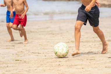Sahilde futbol oynayan çocuklar yazın başlangıcının tadını çıkarıyorlar. Tanınmayan insanlar. Yaz tatili kavramı.