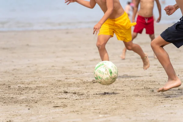 Sahilde futbol oynayan çocuklar yazın başlangıcının tadını çıkarıyorlar. Tanınmayan insanlar. Yaz tatili kavramı.
