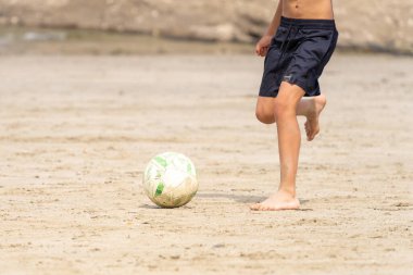 Çocuk kumsalda futbol topunu tekmelemek üzere. Tanınmayan insanlar. Yaz tatili kavramı. 