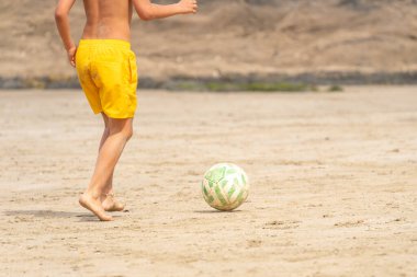 Kumsalda futbol oynayan sarı mayo giyen bir çocuk. Tanınmayan insanlar. Yaz tatili kavramı. 