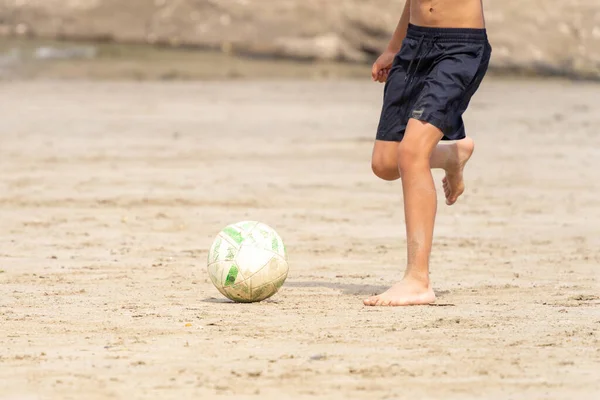 Boy about to kick a soccer ball on the beach sand. Unrecognizable people. Summer vacation concept. 