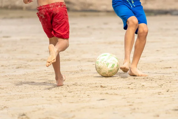 Sahilde futbol oynayan çocuklar yazın başlangıcının tadını çıkarıyorlar. Tanınmayan insanlar. Yaz tatili kavramı.
