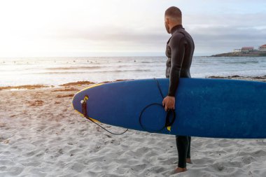 Surfer carrying the surfboard while looking at other surfers before entering the sea to surf. High quality photo