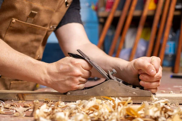 Carpenter\'s hands planing a plank of wood with a hand plane, workplace.