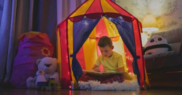かわいい男の子は夜に本を読んでいるテントの中で — ストック動画