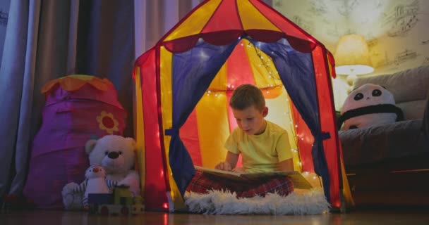 Милый Мальчик Читает Книгу Вечером Палатке — стоковое видео