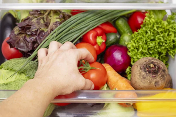 Mans hand is opening drawer of refrigerator with vegetables. Healthy and right food.