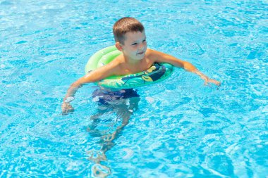 Şişme lastik çemberin üzerinde havuzda yüzen komik çocuk. Çocuk bilardoda oynuyor. Yaz tatili ve tatil konsepti.