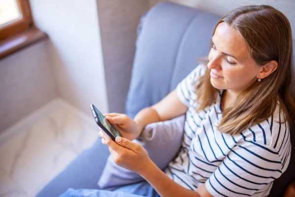 Jovem Feliz Está Usando Telefone Celular Enquanto Está Sentado Sofá — Fotografia de Stock