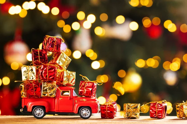 赤いレトロなおもちゃのトラックはクリスマスライトとクリスマスツリーの背景に贈り物を運びます 商品のお届けとグリーティングカードのコンセプト新年明けましておめでとうございます — ストック写真