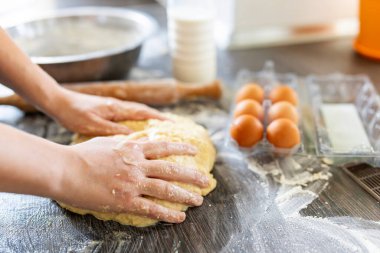 Dişi eller merdane, yumurta ve süt şişesinin yanındaki ahşap masada pişirmek için hamur yapıyor. Mutfak, yemek pişirme, pişirme konsepti