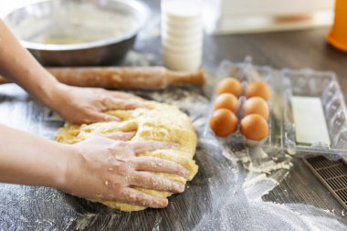 Dişi eller merdane, yumurta ve süt şişesinin yanındaki ahşap masada pişirmek için hamur yapıyor. Mutfak, yemek pişirme, pişirme konsepti