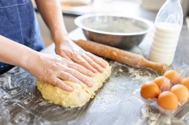 Dişi eller merdane, yumurta ve süt şişesinin yanındaki ahşap masada pişirmek için hamur yapıyor. Mutfak, yemek pişirme, pişirme konsepti