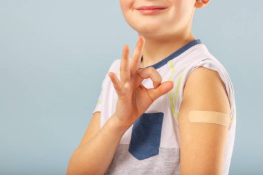 Çocukların aşılanması için. Mutlu aşılanmış çocuk iyi bir jest yapıyor ve aşı olduktan sonra koluna bandaj yapıştırıyor. Çocuklar ve covid-19 önleme, antiviral bağışıklık.