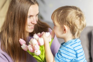 Güzel sarışın çocuk, annesine bir buket lale veriyor. Anneler gününde onu tebrik ediyor ve tatilini evde kutluyor..