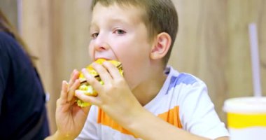 Fast food restoranında büyük hamburger yiyen sevimli çocuk. Çocuklar için sağlıksız bir yemek. Abur cubur. Aşırı kilolu çocuk
