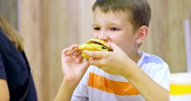 Fast food restoranında büyük hamburger yiyen sevimli çocuk. Çocuklar için sağlıksız bir yemek. Abur cubur. Aşırı kilolu çocuk