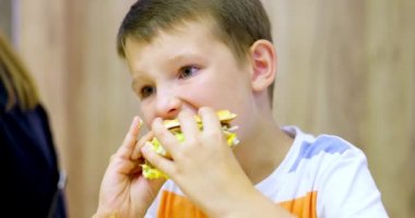 Fast food restoranında büyük hamburger yiyen sevimli çocuk. Çocuklar için sağlıksız bir yemek. Abur cubur. Aşırı kilolu çocuk