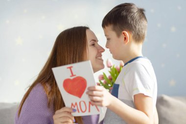 Anneler Günün kutlu olsun! Çocuk evlat annesini tebrik eder ve ona bir kartpostal ve bir buket lale verir..
